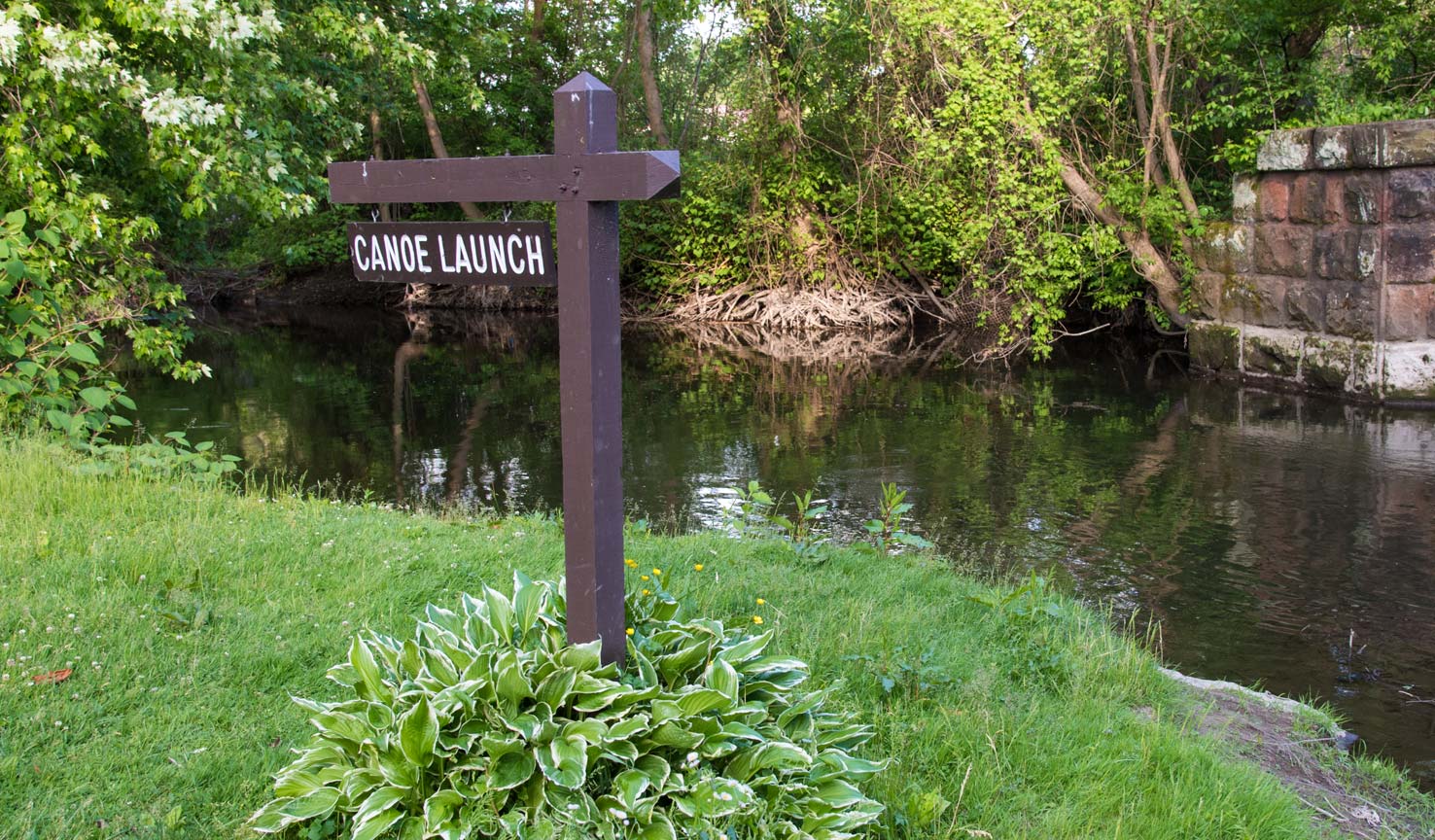 A sign in front of a creek with the words 'canoe launch'